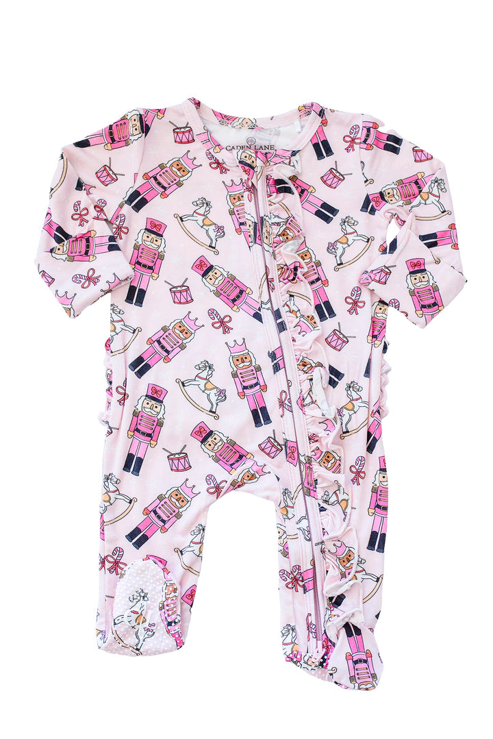Flat lay of Caden Lane's pink toy soldier print ruffle zip-up pajamas, featuring nutcrackers and rocking horses.