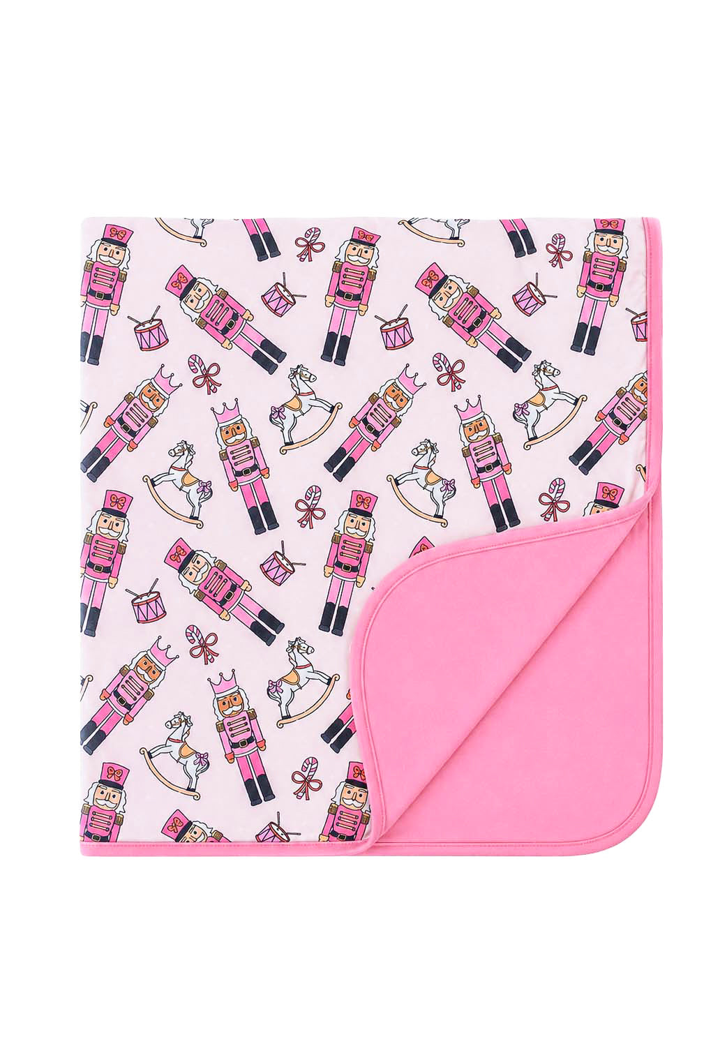Caden Lane's pink toy soldier print baby blanket featuring nutcrackers, rocking horses, drums, and candy canes, with a solid pink reverse side, folded to show both sides.