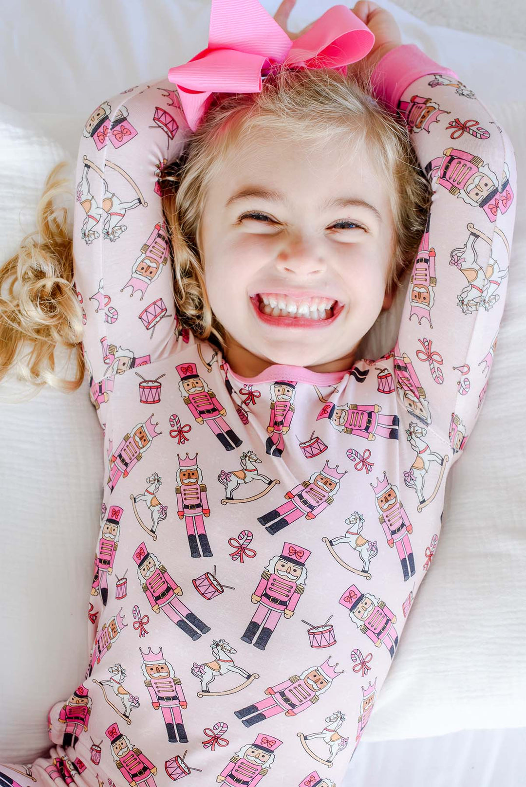 Close-up of girl laughing while wearing Caden Lane's pink toy soldier print pajamas, featuring nutcrackers, rocking horses, and candy canes.