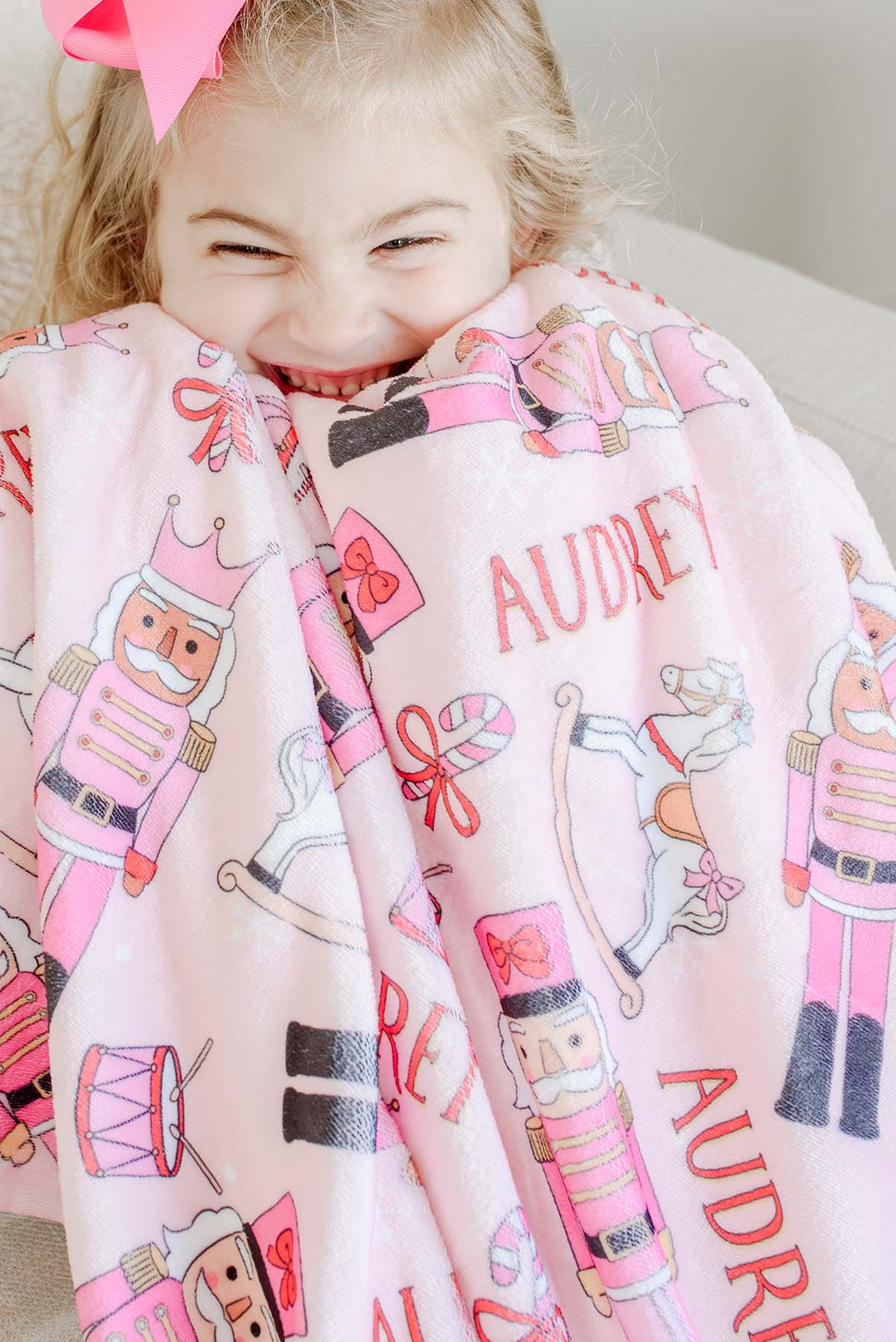 Close-up of a girl smiling while wrapped in Caden Lane's pink toy soldier print blanket personalized with the name "Audrey."