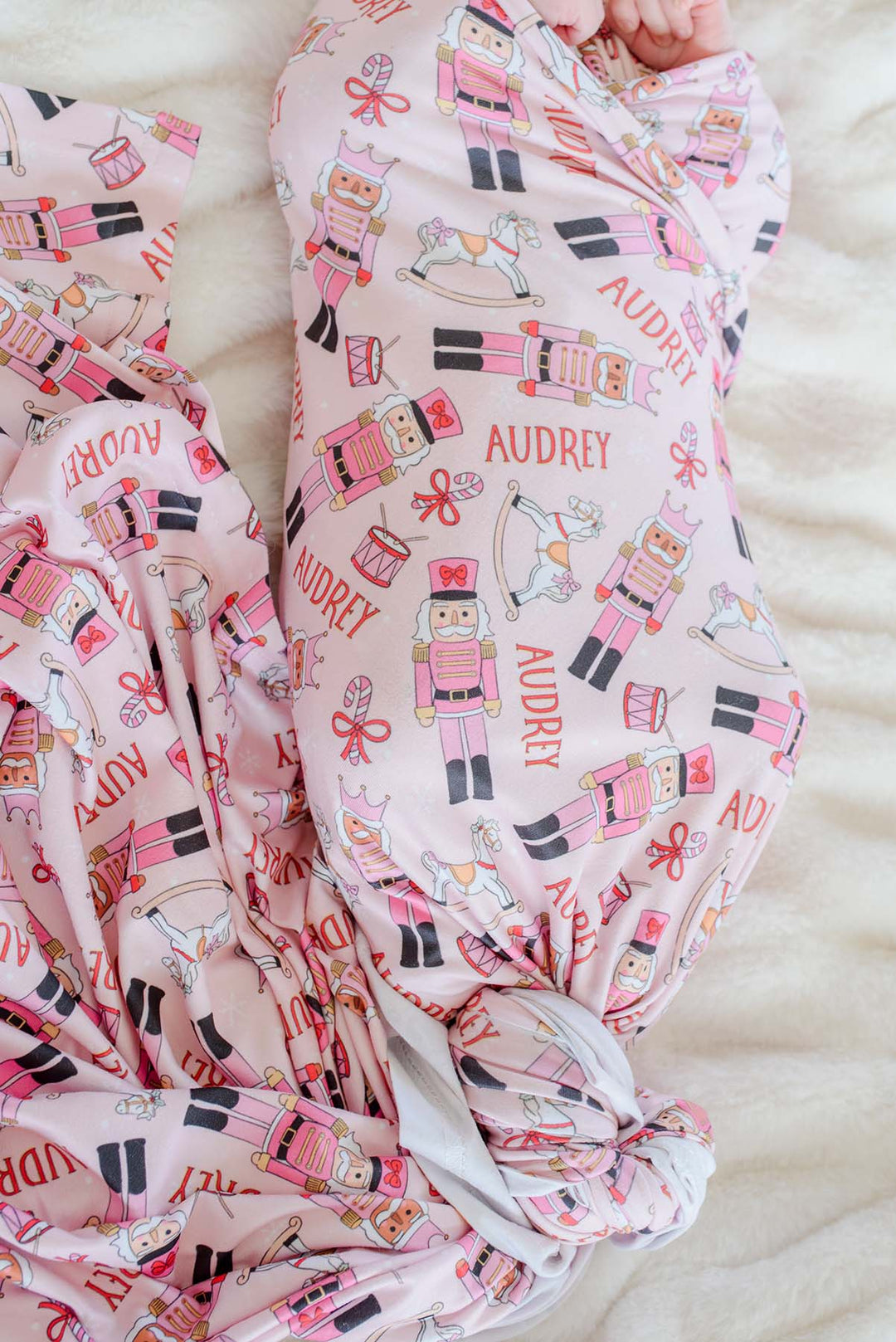 Close-up of Caden Lane's pink toy soldier print blanket personalized with the name "Audrey," featuring nutcrackers, rocking horses, and candy canes.