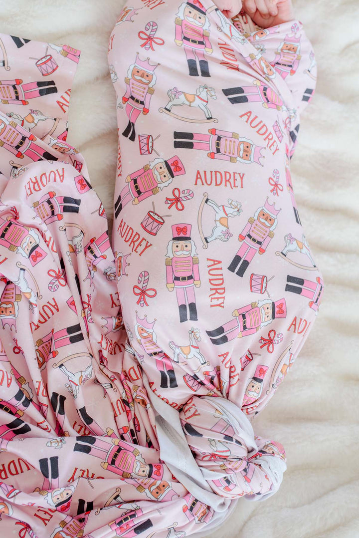 Close-up of Caden Lane's pink toy soldier print blanket personalized with the name "Audrey," featuring nutcrackers, rocking horses, and candy canes.