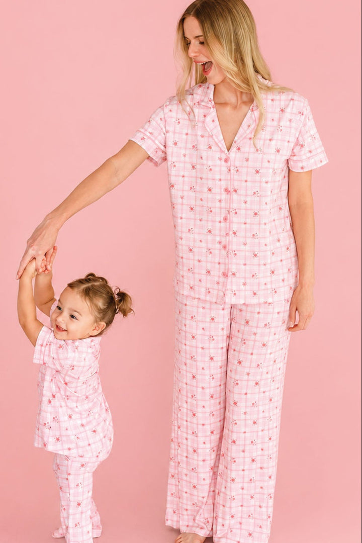 A woman and a young girl wearing Caden Lane matching pink patterned pajamas, with the woman holding the child's hand against a solid pink studio background.