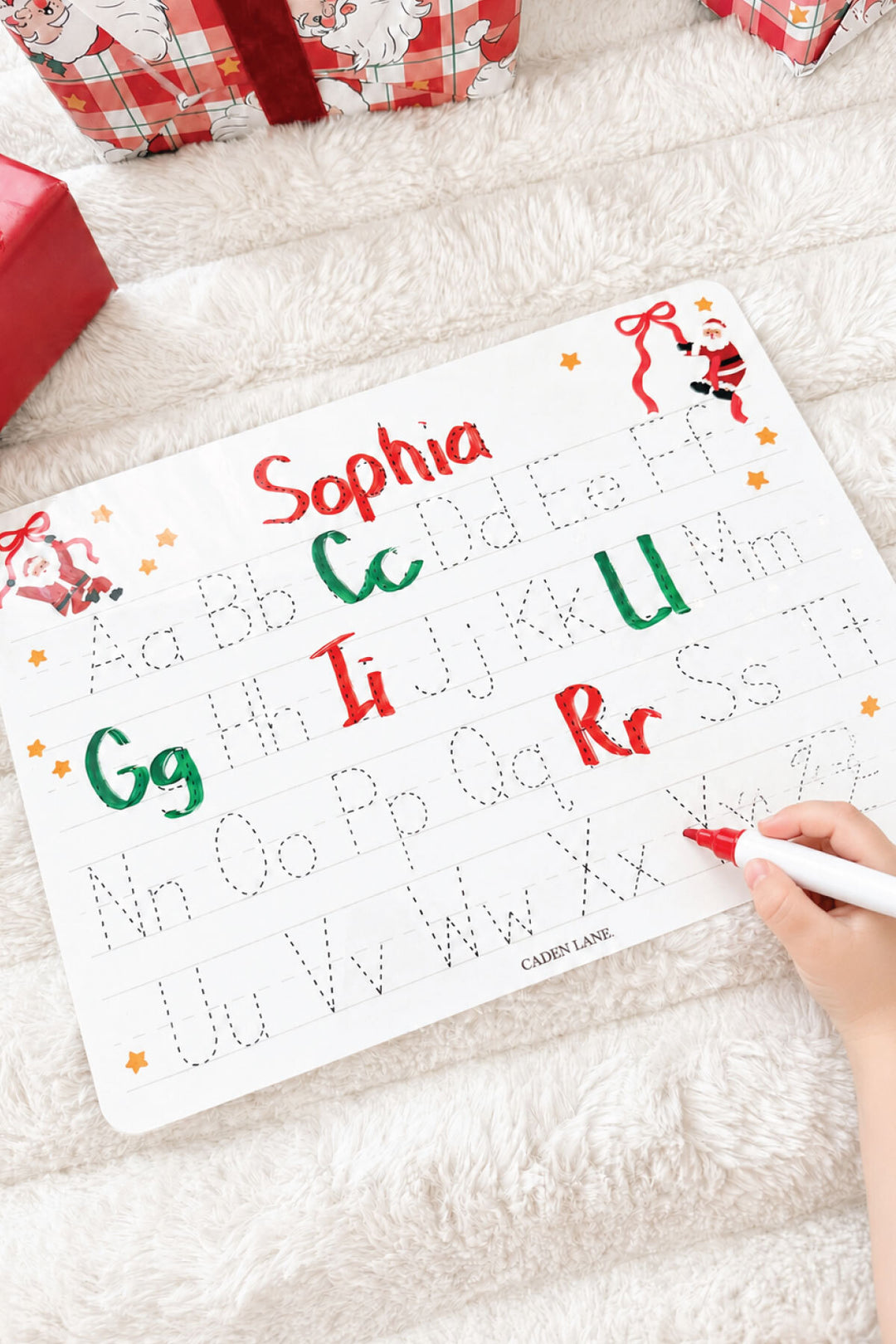 Caden Lane Personalized Kids' Christmas Whiteboard in the Jolly Ribbons print featuring a custom name, reusable dry-erase handwriting practice board with festive Santa and ribbon design for holiday learning and personalized Christmas gifts.