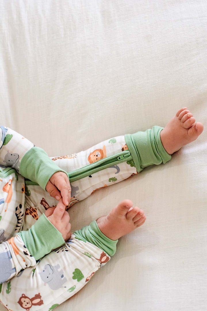 Overhead close-up of a baby's legs in a Caden Lane Wild Child convertible zip romper, showing the green leg zipper and fold-over cuffs.