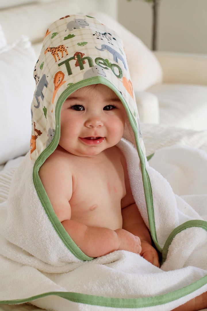 Close-up of a grinning baby in a Caden Lane white terry hooded towel with green trim and a Wild Child print hood embroidered in green with "Theo."