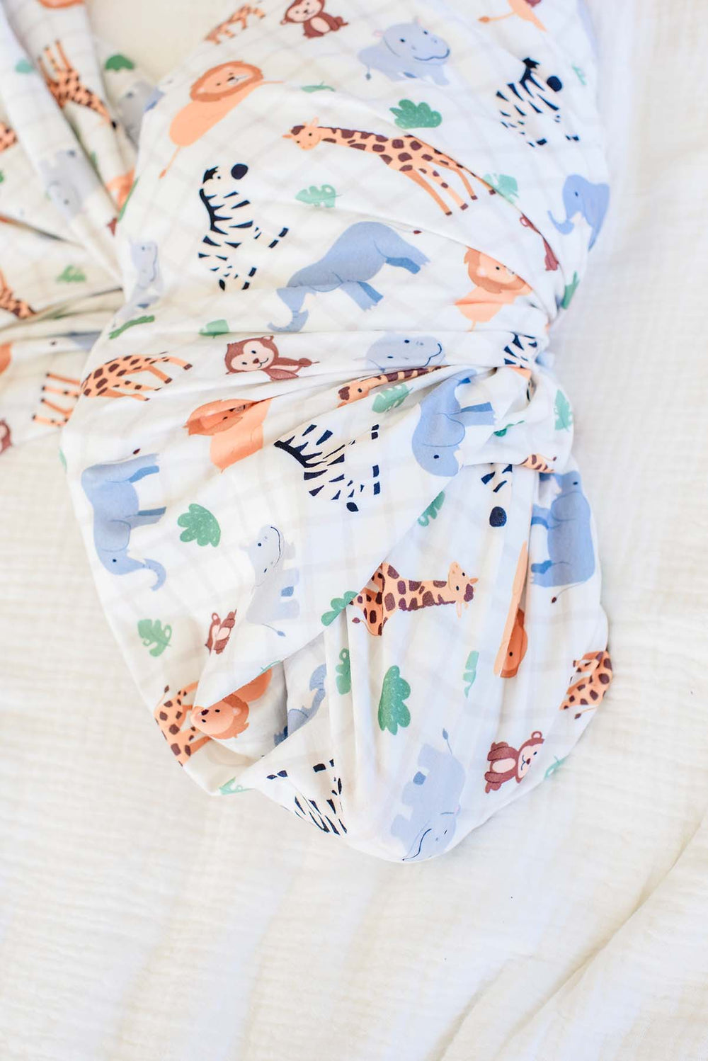 Close-up of the gathered bottom of a Caden Lane swaddle blanket in a Wild Child print featuring giraffes, elephants, zebras, lions and hippos on cream plaid.