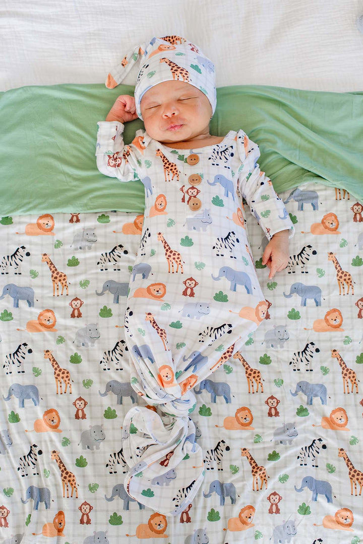Overhead view of a sleeping newborn wearing a Caden Lane knotted gown and matching knot hat in a Wild Child print, lying on a Wild Child blanket folded back to show its sage green reverse.