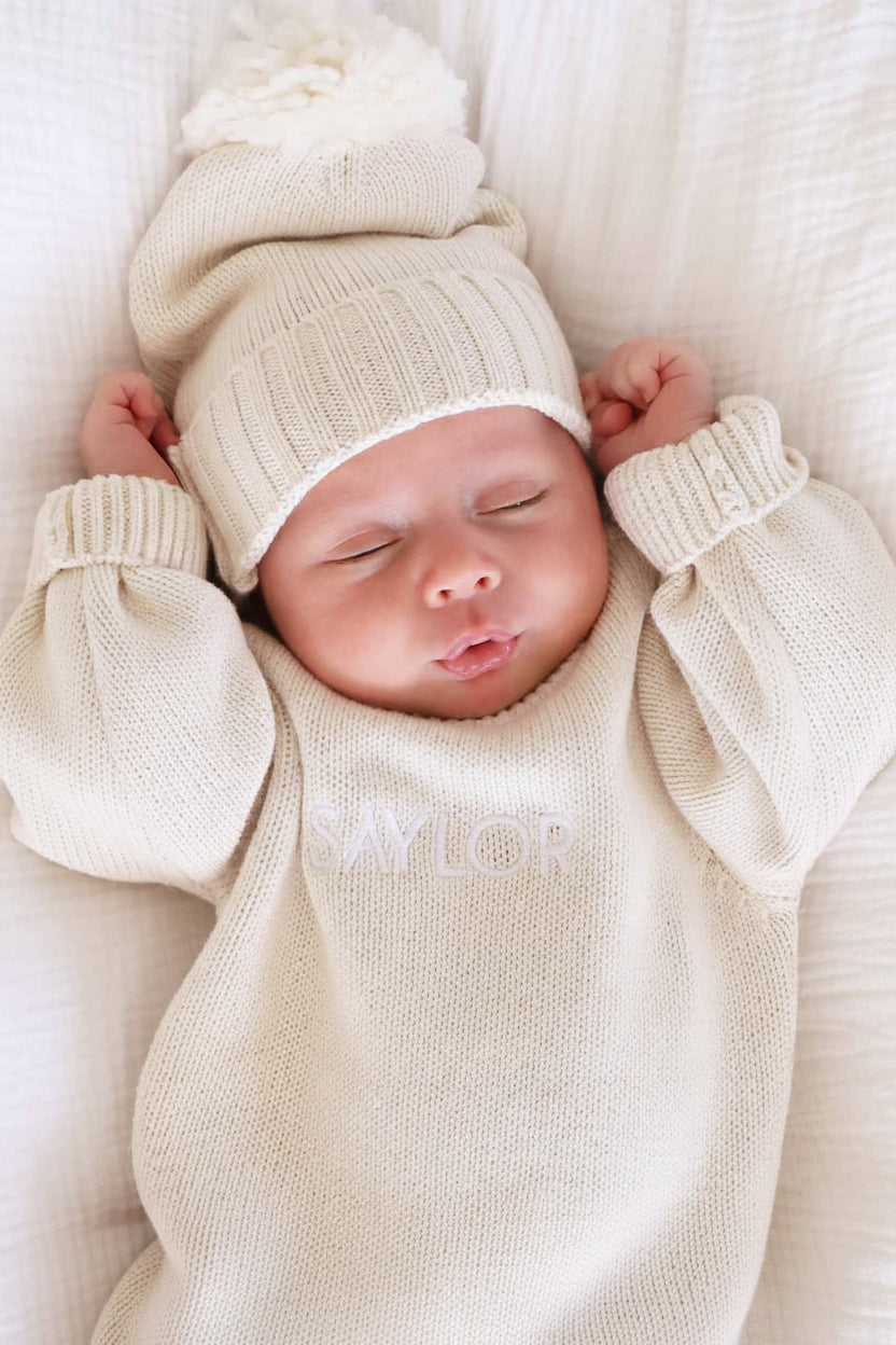 long sleeve beige personalized sweater romper for babies embroidered with name with matching pom pom beanie 