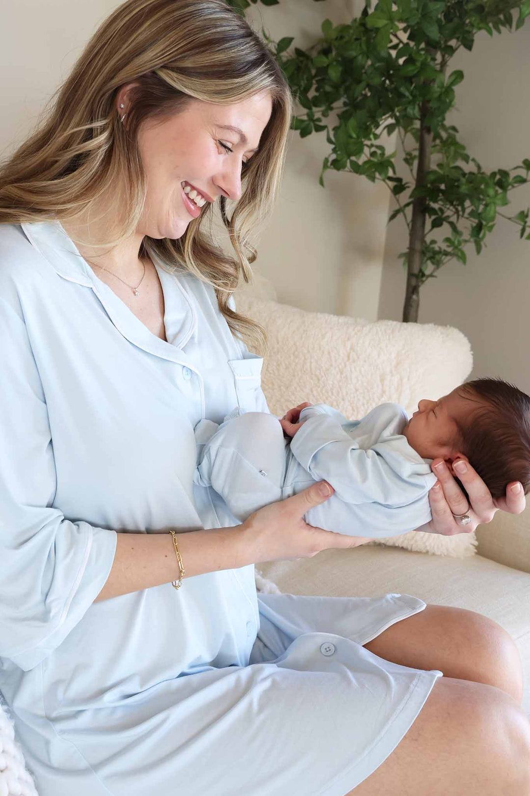 mom wearing light blue labor & delivery gown holding baby out in front of her in matching footie 