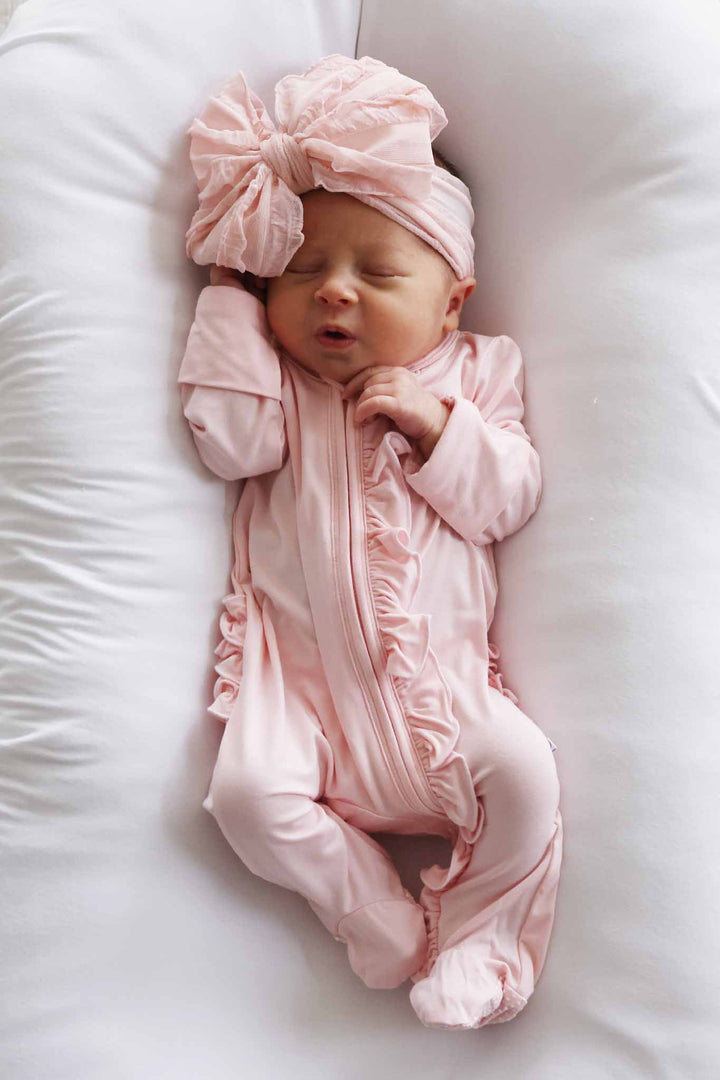 baby girl laying down wearing the baby pink ruffle zipper footie with matching ruffle bow 