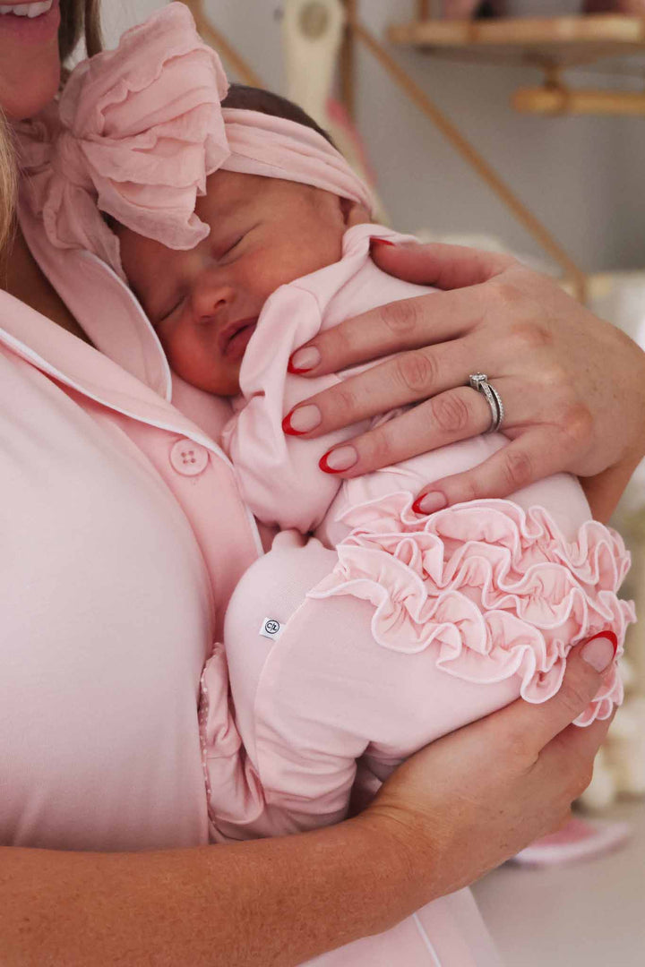 mom holding baby girl wearing a light pink bamboo waffle ruffle zipper footie 