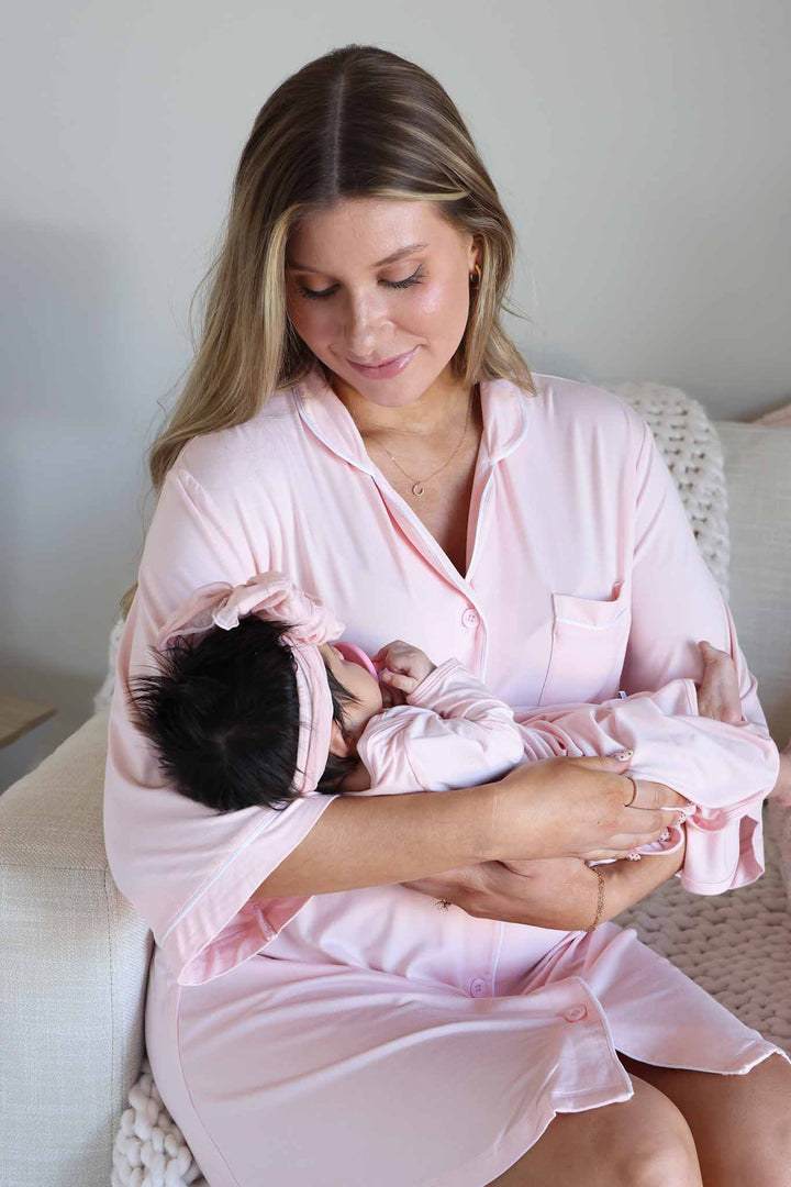 mom in baby pink labor & delivery gown looking down at baby in matching knot gown 
