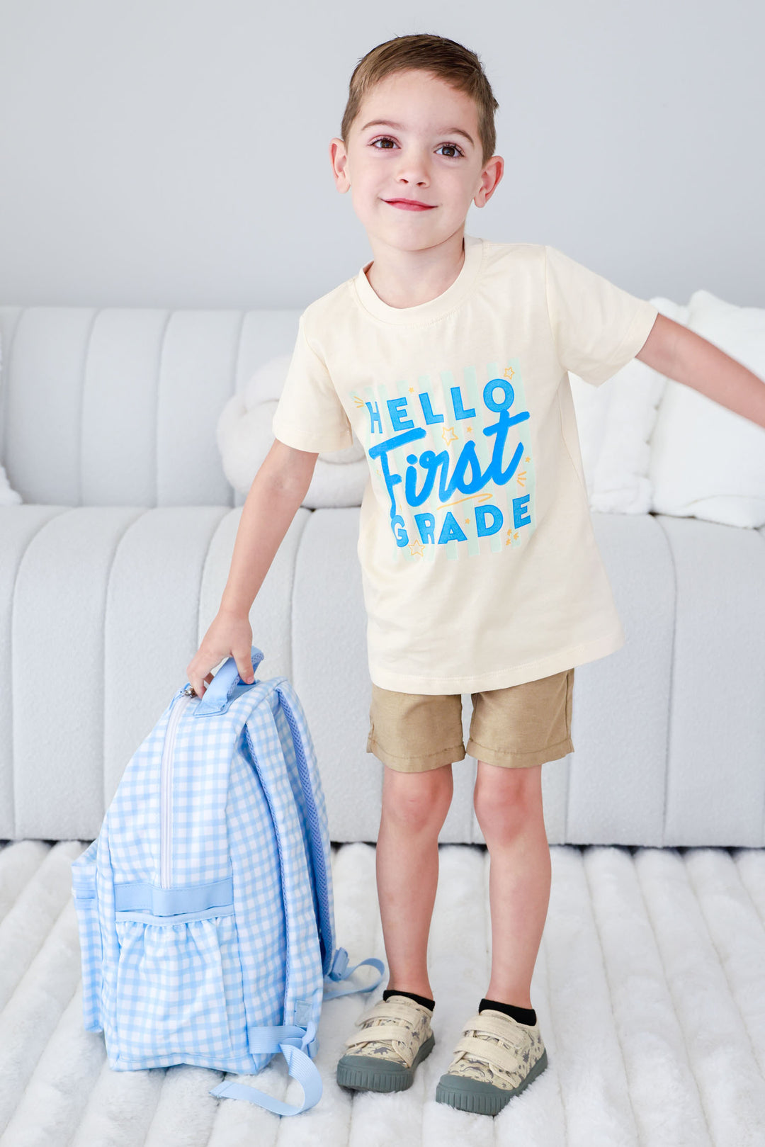 boy in hello first grade t-shirt holding blue gingham backpack