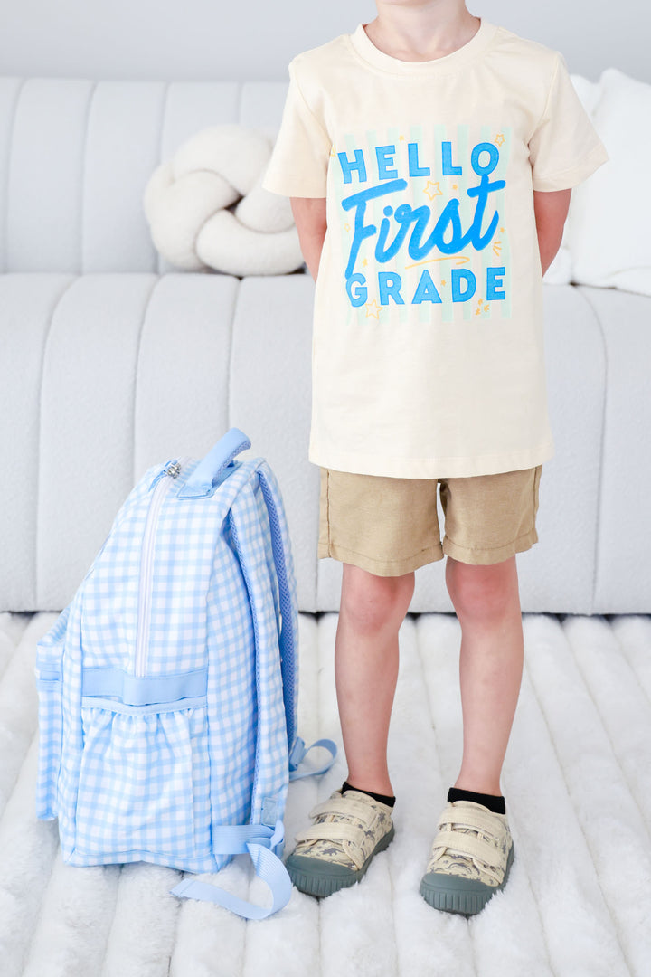 boy in first day of school outfit standing next to blue gingham backpack 