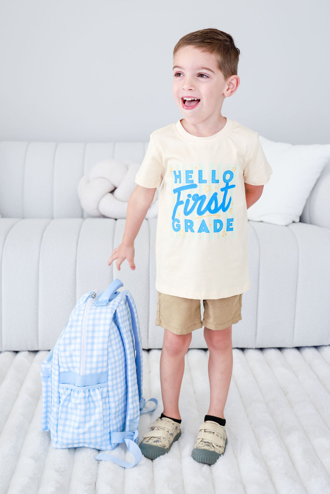 boy standing next to blue gingham backpack in back to school shirt 