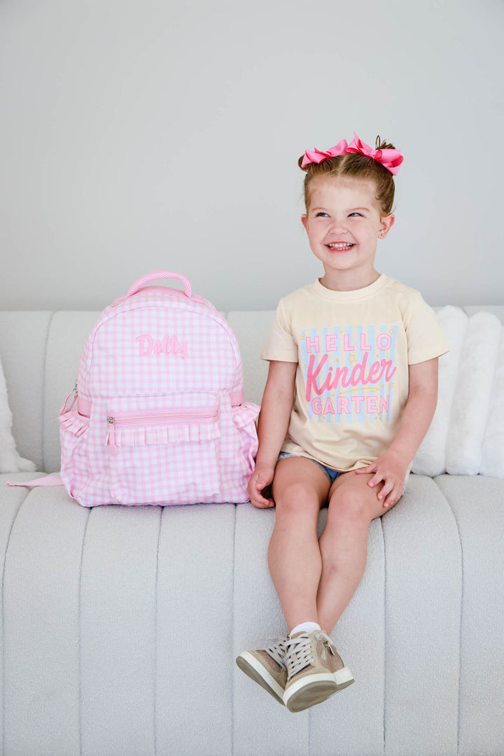 girl sitting on the couch in pink gingham embroidered backpack with a back to school t-shirt
