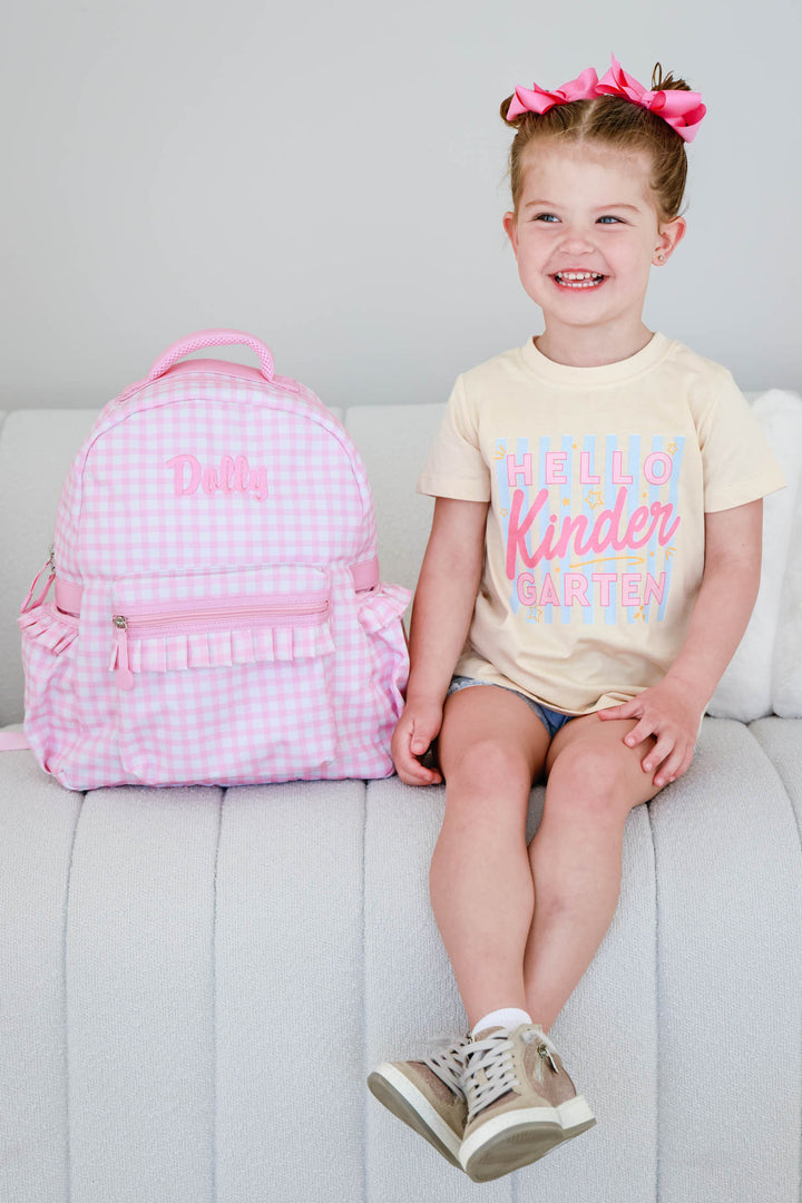 girl sitting on the couch next to pink gingham embroidered backpack 