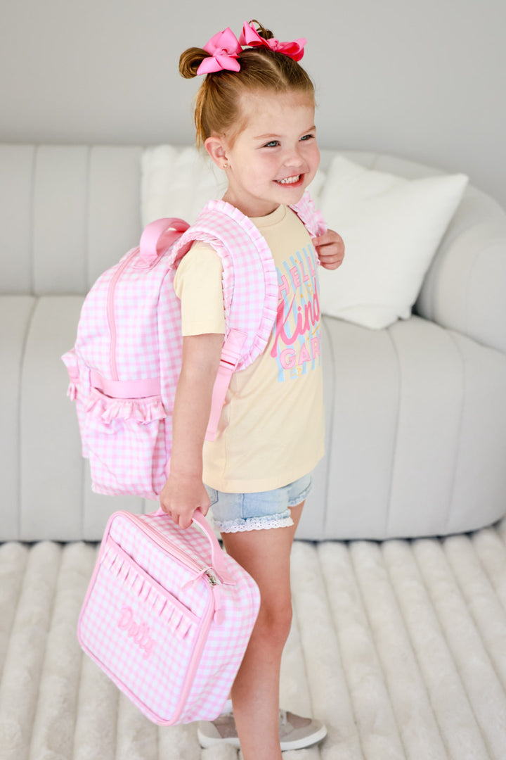 girl wearing back to school t-shirt holding pink gingham embroidered lunchbox with matching backpack 