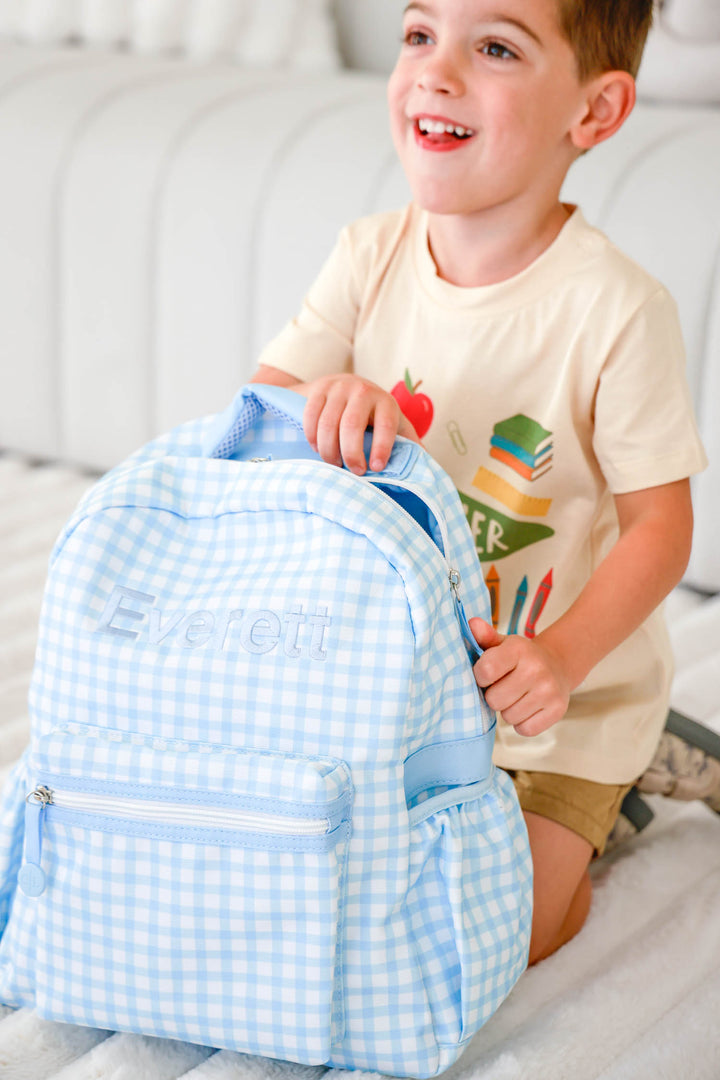 boy kneeling next to blue gingham embroidered backpack 
