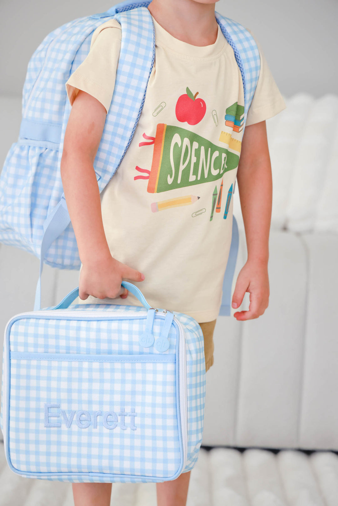 boy holding blue gingham embroidered lunchbox with matching backpack and t-shirt