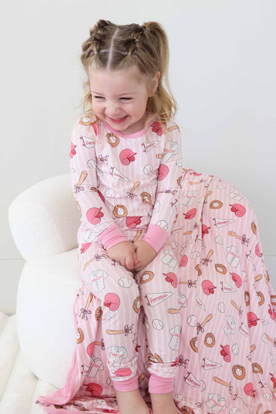 smiling girl sitting on chair with hands in lap in pink baseball pajama set 