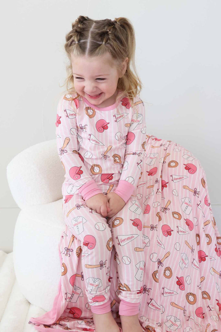smiling girl sitting on chair with hands in lap in pink baseball pajama set 