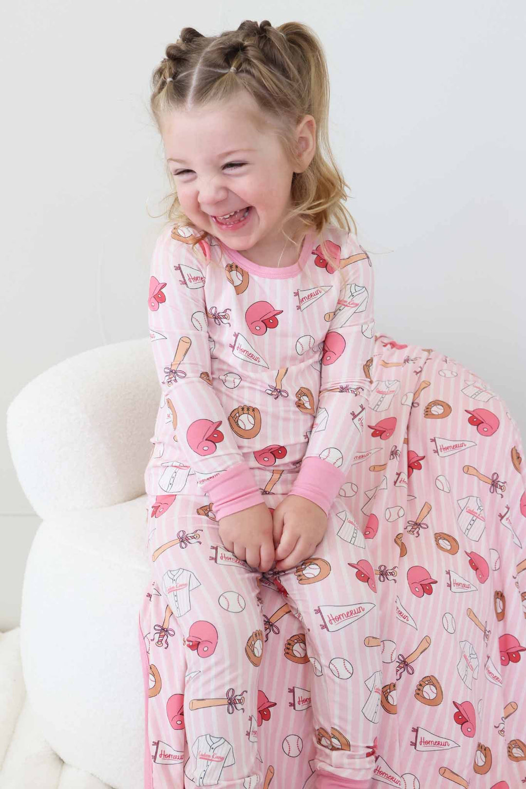 happy girl in ballpark babes two piece pajama set sitting on matching bamboo blanket 
