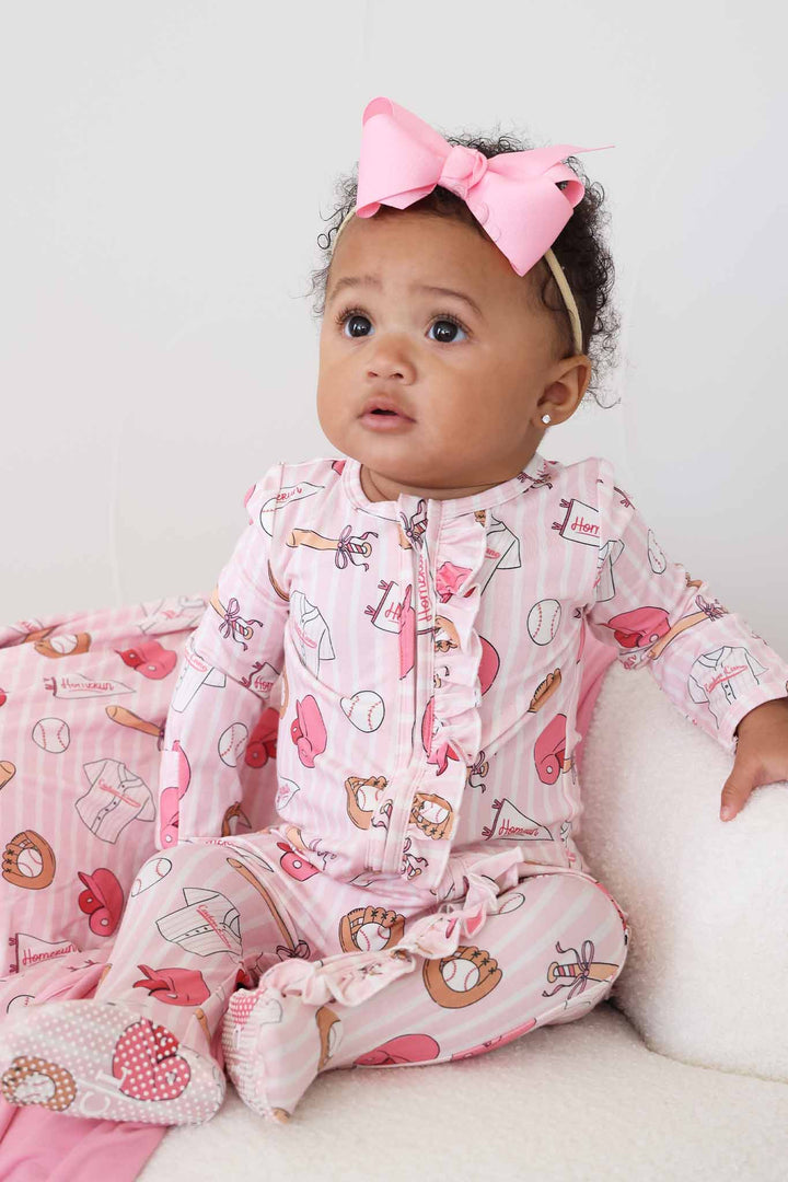 baby girl sitting on chair in ballpark babes ruffle zipper footie pajama with a matching pink ribbon bow headband 