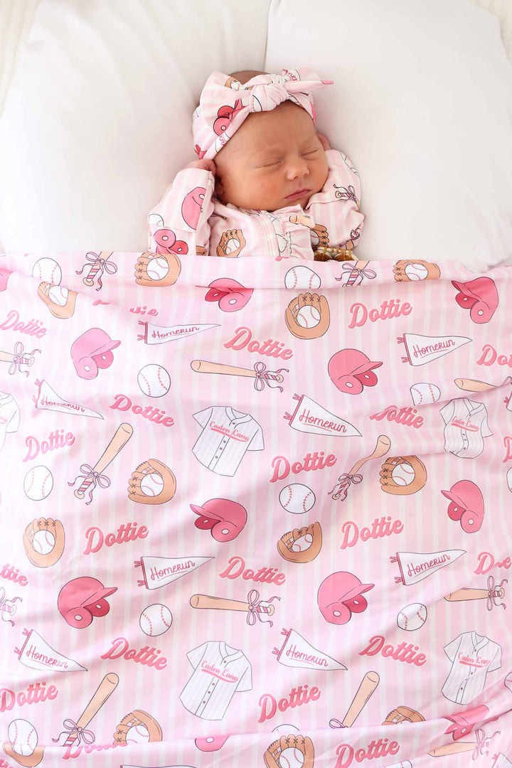 baby girl covered in ballpark babes personalized swaddle blanket wearing a matching ruffle footie 