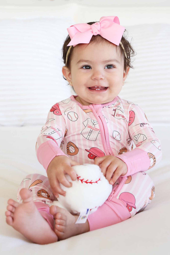 sitting baby girl in pink ballpark babes convertible zip romper holding a stuffed baseball 