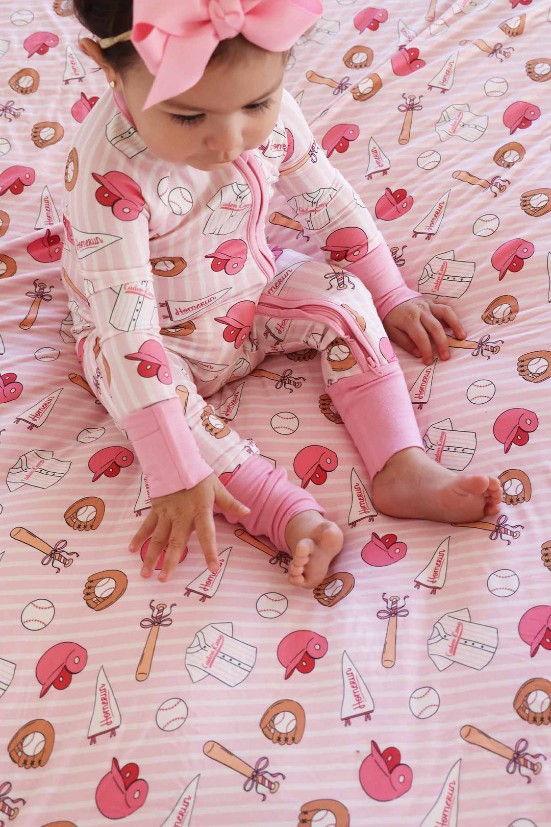 baby girl sitting on ballpark babes bamboo blanket wearing a matching zip romper pajama and pink ribbon bow headband 