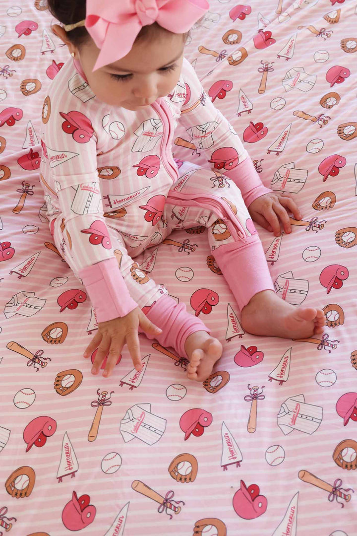 baby girl sitting on ballpark babes bamboo blanket wearing a matching zip romper pajama and pink ribbon bow headband 