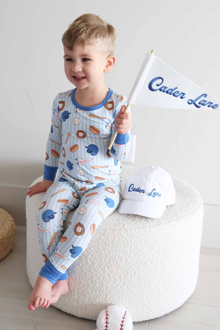 boy sitting on ottoman in baseball two piece pajama set holding a banner with a baseball cap next to him 