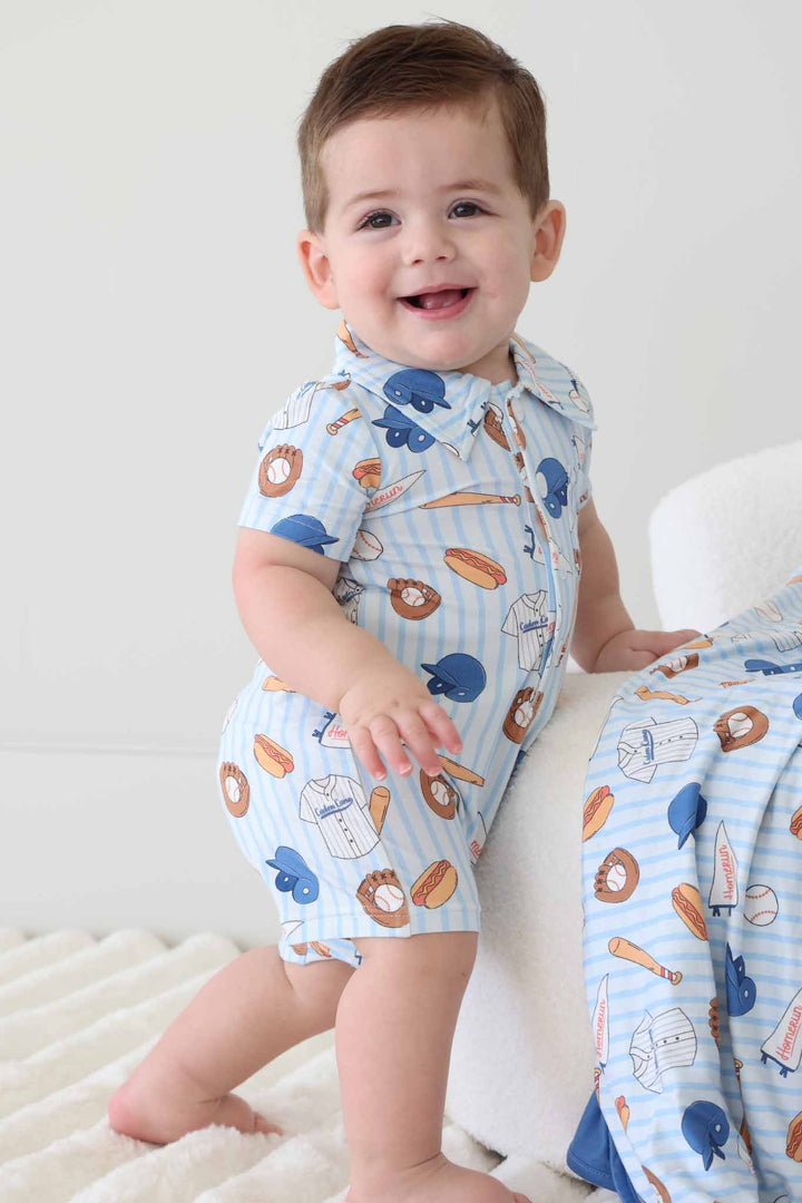 baby boy standing leaning against ottoman in ballpark bros collared button up romper 