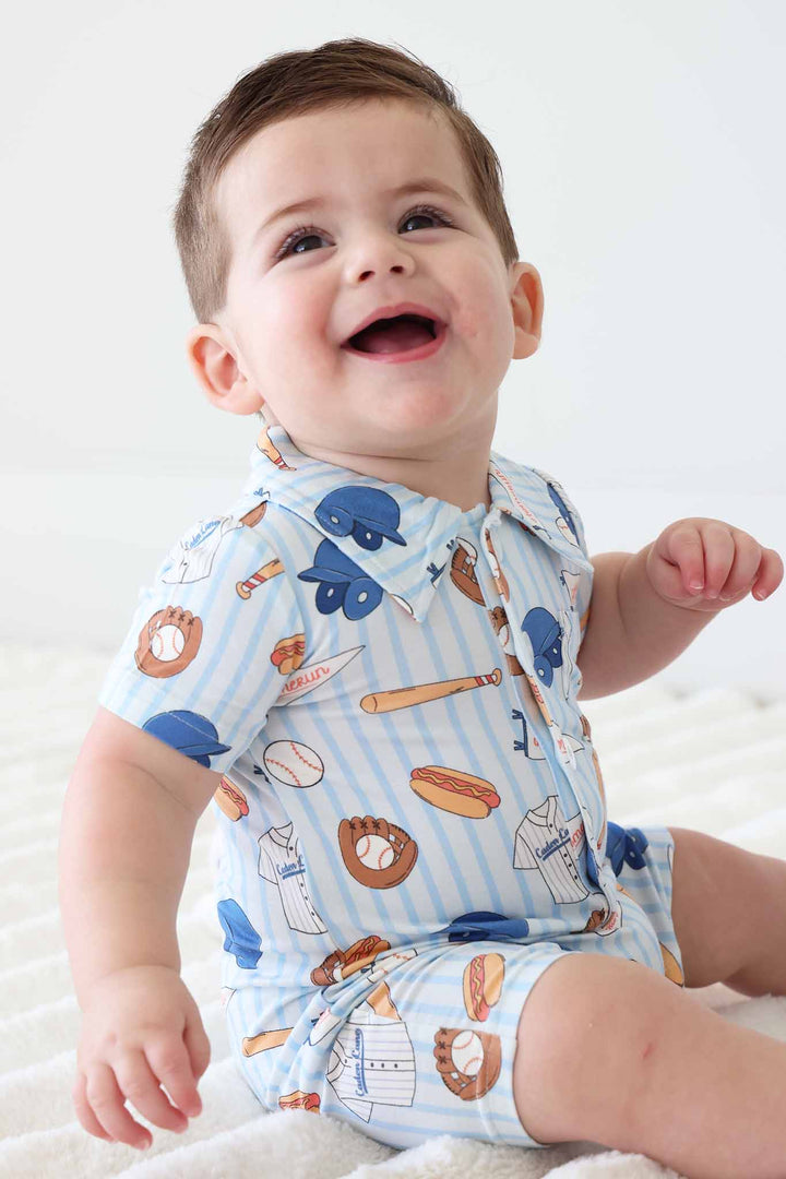 sitting baby boy smiling and looking up wearing the ballpark bros collared button romper 