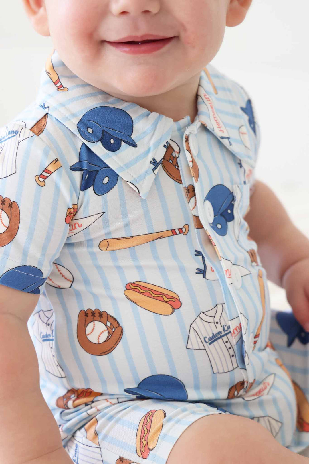 closeup of collared button romper for boys in blue striped baseball print with bats, hotdogs, helmets, jerseys and more 