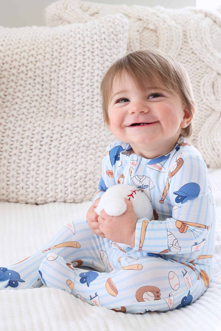 baby boy hugging stuffed baseball wearing long sleeve baseball themed footie pajama 