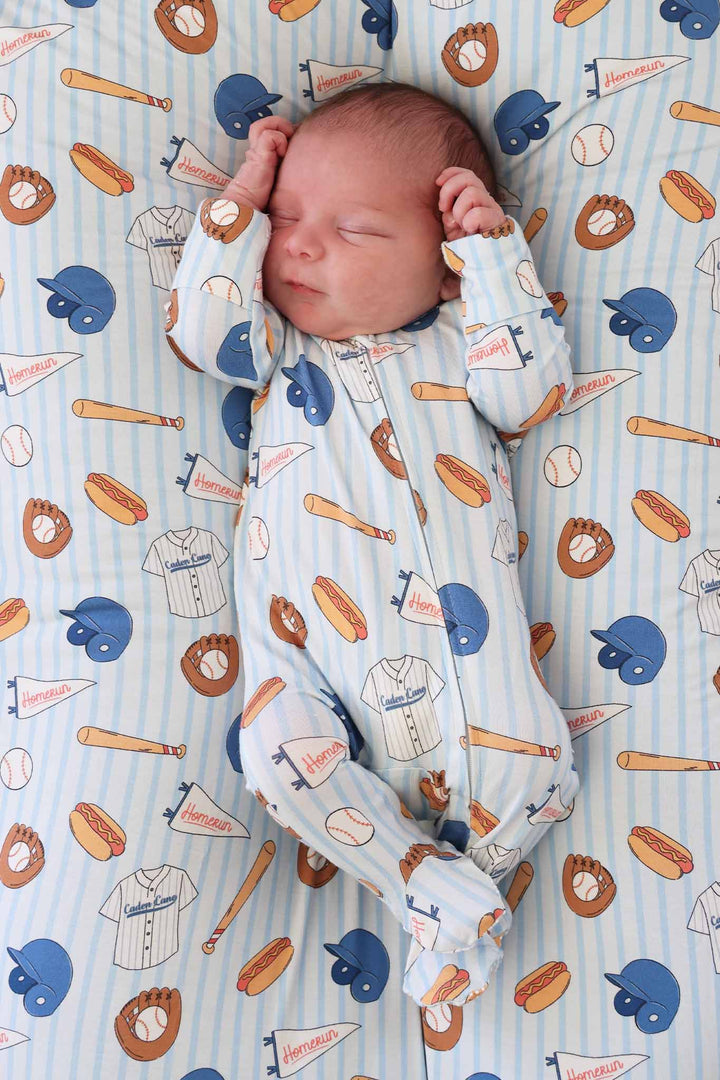 newborn boy laying on blue striped baseball themed blanket with a matching zipper footie 