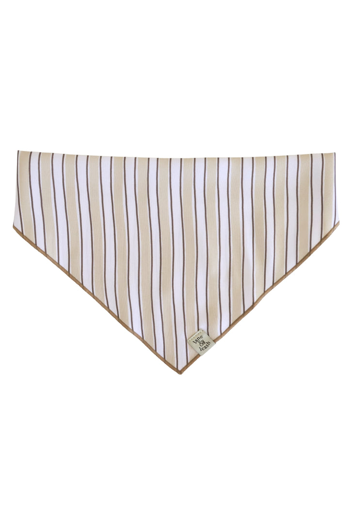 Flat-lay of embroidered pet bandana in Biscuit Stripe pattern showing triangle shape with tan and white vertical stripes and a woven label at the tip