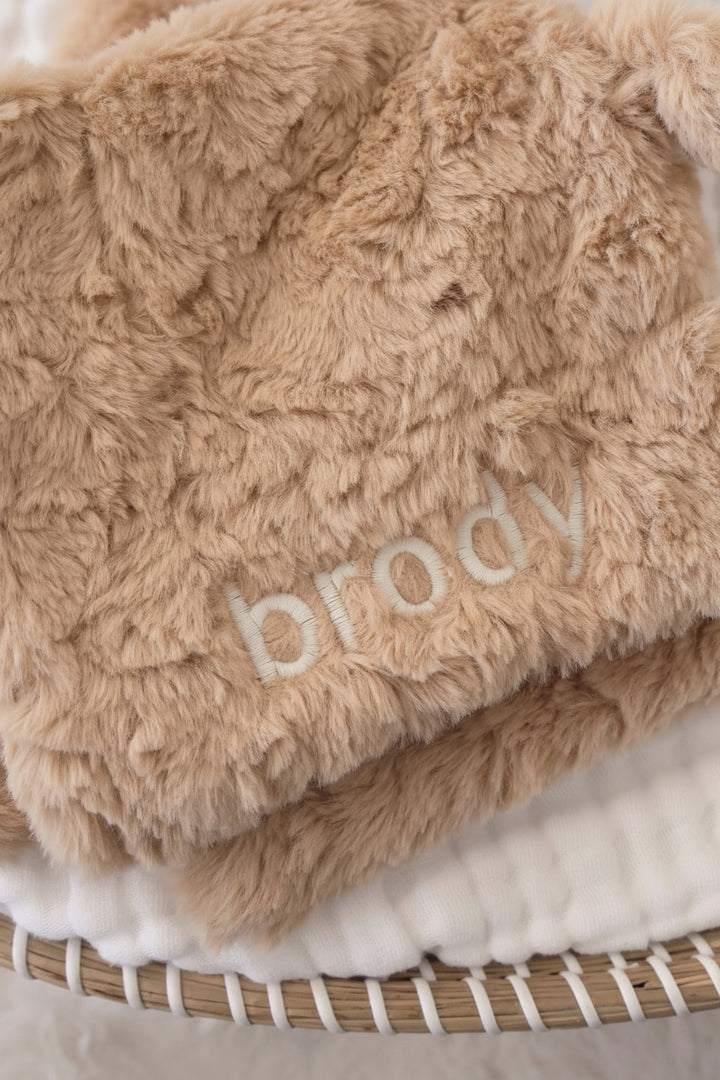 closeup of furry brown teddy bear lovey for babies embroidered with name in white thread with block font 