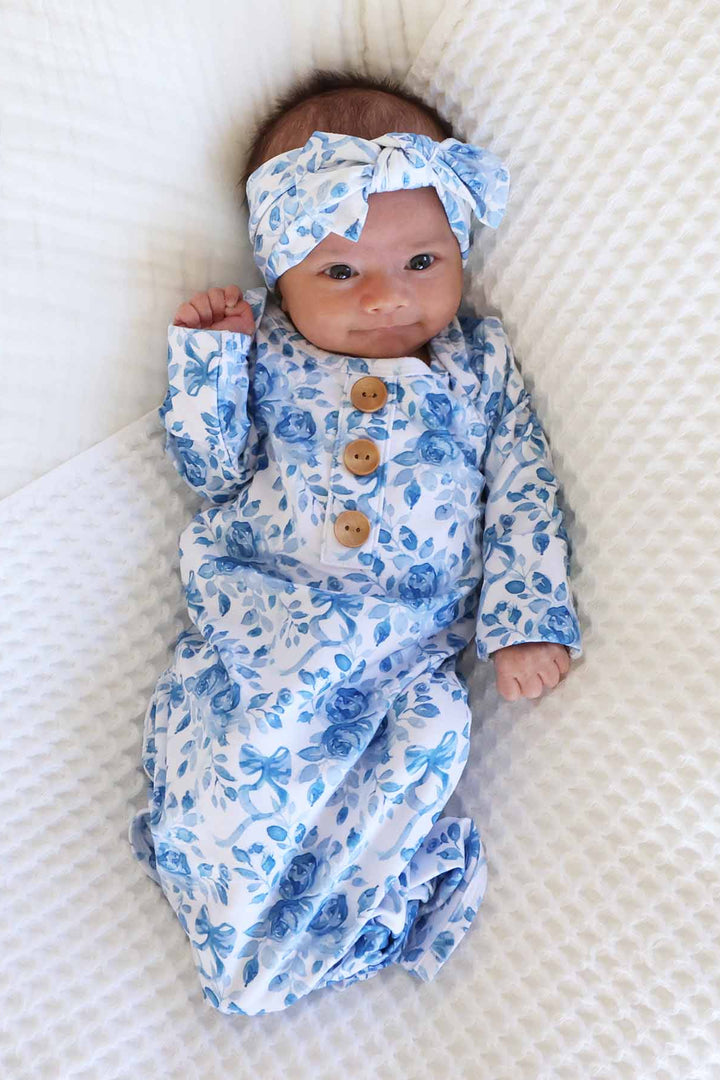 newborn baby girl wearing a blue and white floral and bow long sleeve knot gown with matching bow headwrap