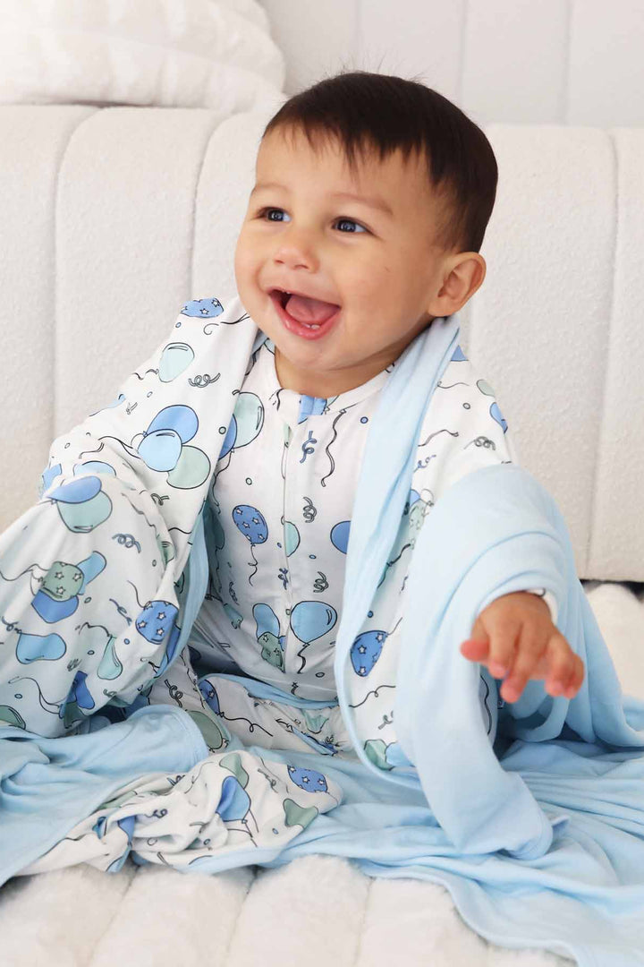 toddler boy with blue and green balloon bamboo blanket draped over him 