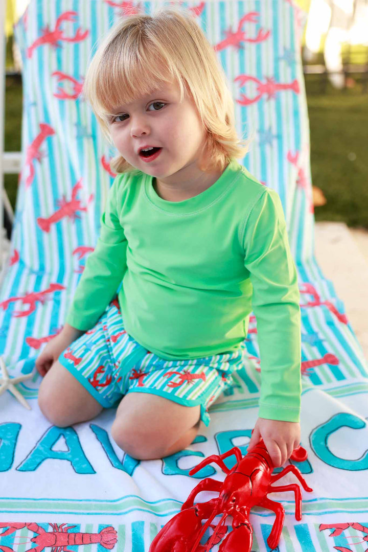 boy kneeling on beach chair wearing lobster swim trunks and matching long sleeve rash guard shirt 
