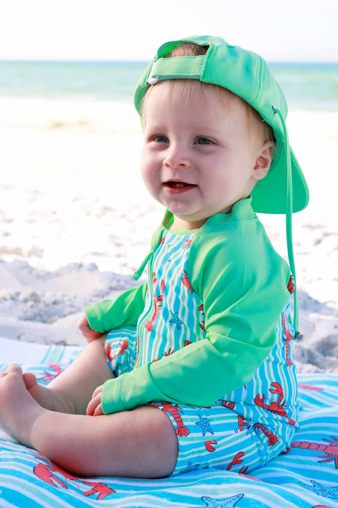 baby boy sitting on beach towel in blue pinch me long sleeve swim romper shortie