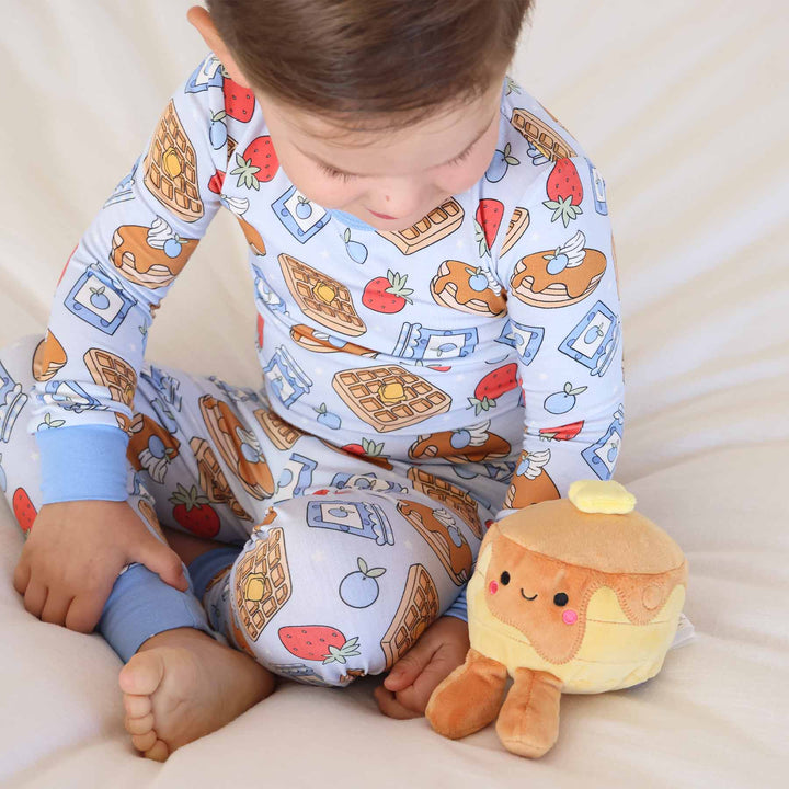 boy sitting on a bed with pancake stuffed animal wearing breakfast themed pajamas