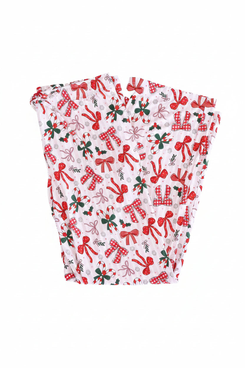 Flat lay of Pajama pants with white and light pink stripes background plus various red bows on top. Unisex Lounge style.