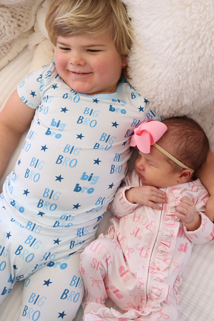 boy in big bro two piece pajama set with his arm around baby sister in little sis ruffle footie pajama 