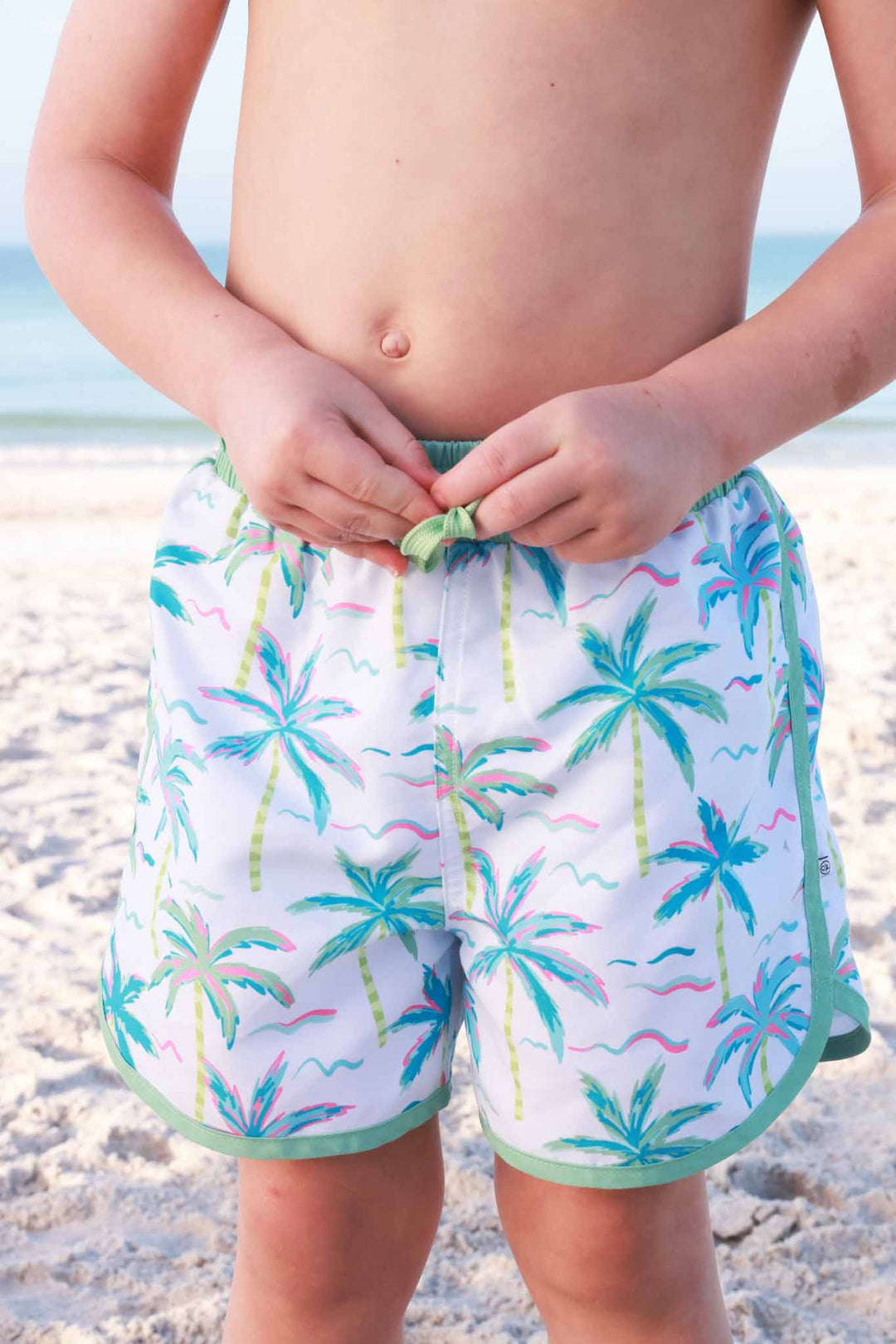 boy wearing neon palm tree swim trunks and tying waistband 