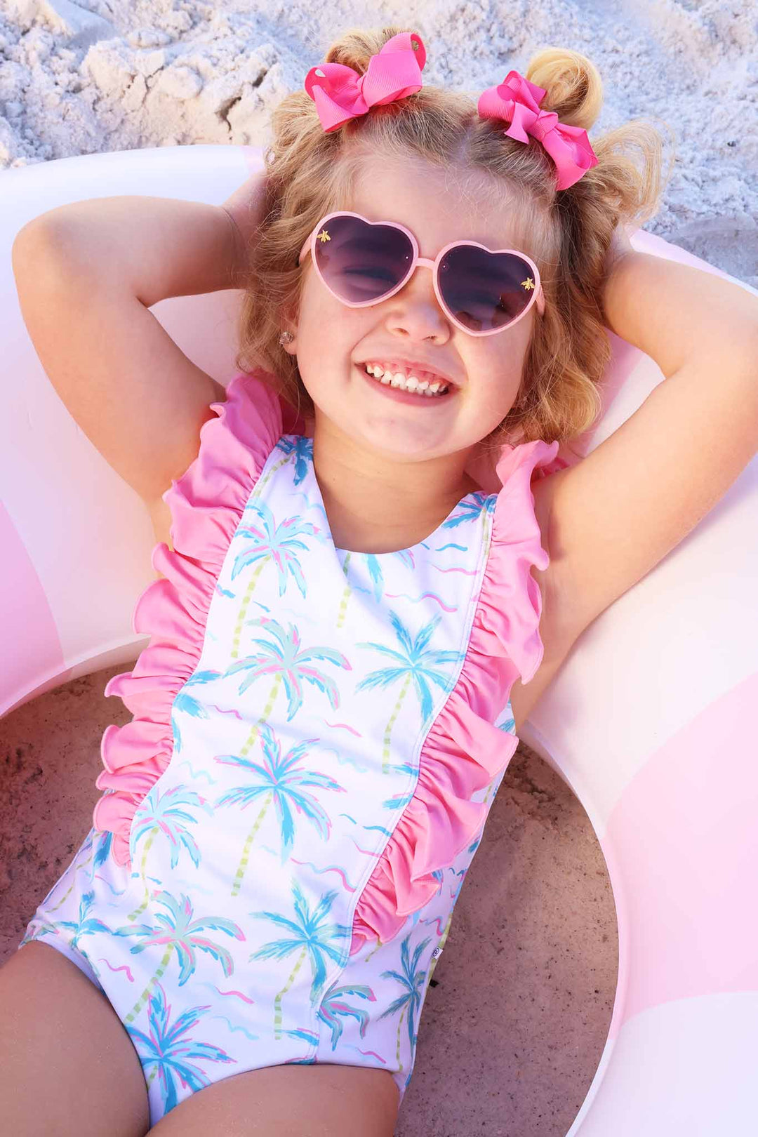 girl laying in inner tube in neon palm tree one piece swimsuit with bright pink ruffles along the front and shoulders